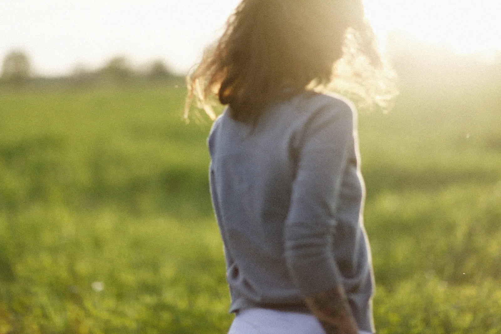 A woman walking away through a sunlit field